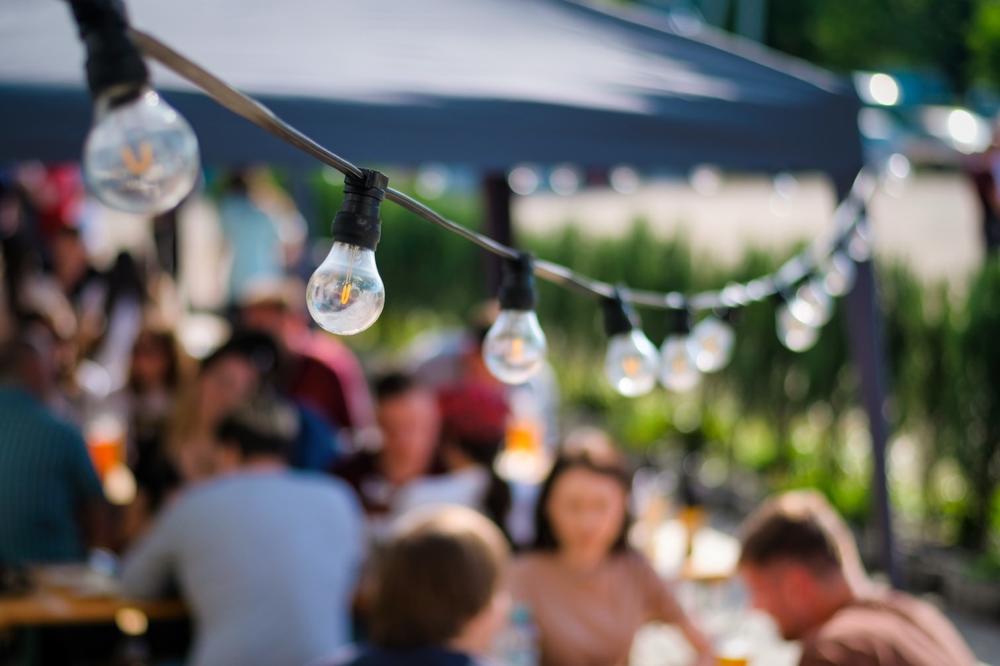 People gathering outdoors under warm string lights